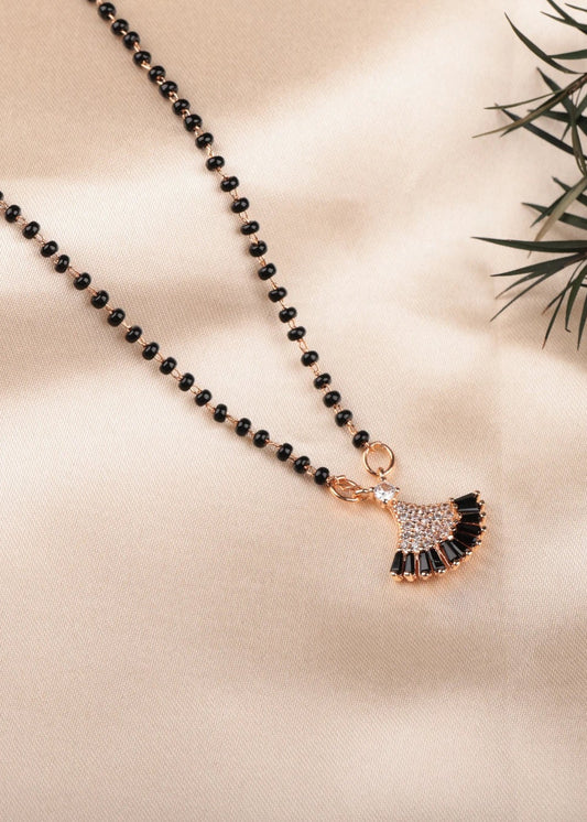 Black beaded necklace with a decorative pendant on a beige surface with green leaves and white flowers.