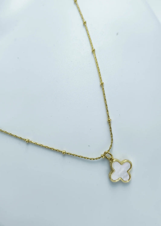 Gold necklace with a clover-shaped pendant on a light gray background