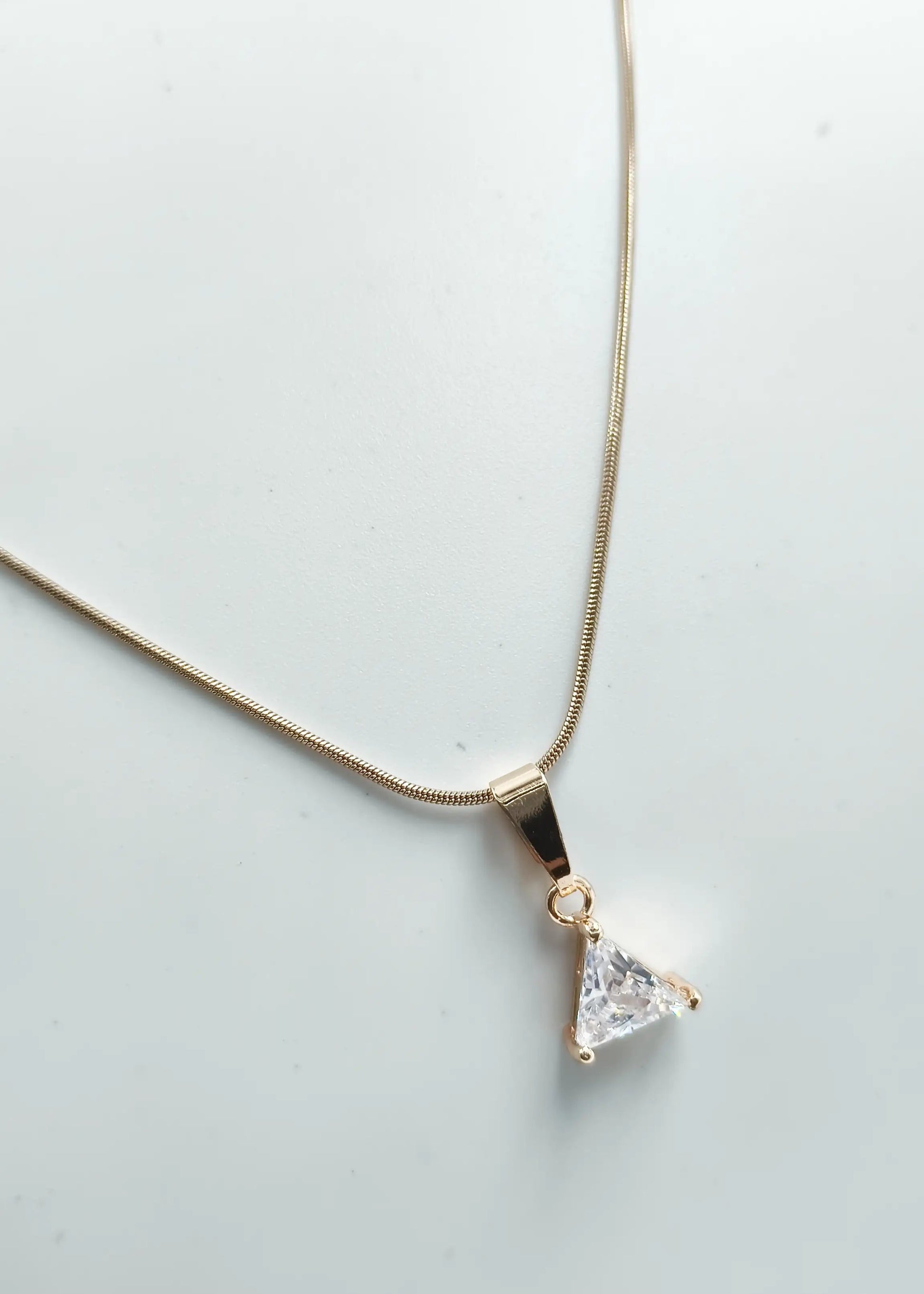 Triangle-shaped diamond pendant on a gold chain against a light gray background