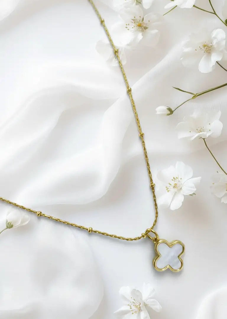 Gold necklace with a clover-shaped pendant on a white fabric background
