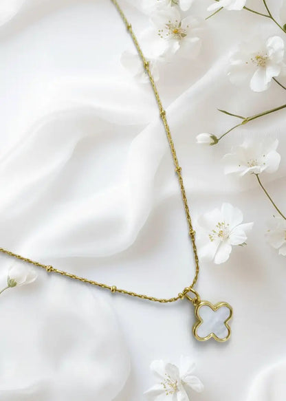Gold necklace with a clover-shaped pendant on a white fabric background