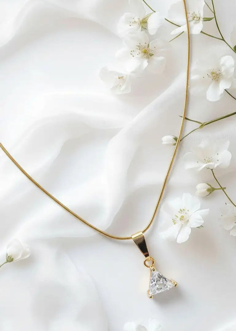 Gold necklace with a triangular pendant on a white fabric background