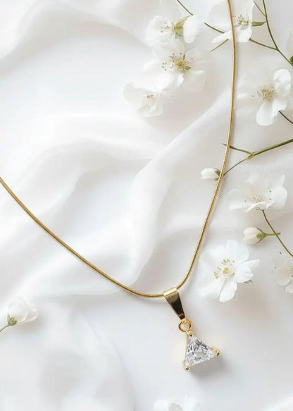 Gold necklace with a triangular pendant on a white fabric background